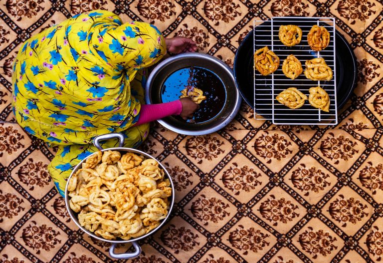 Woman in yellow dress preparing traditional Algerian pastries captured from above.