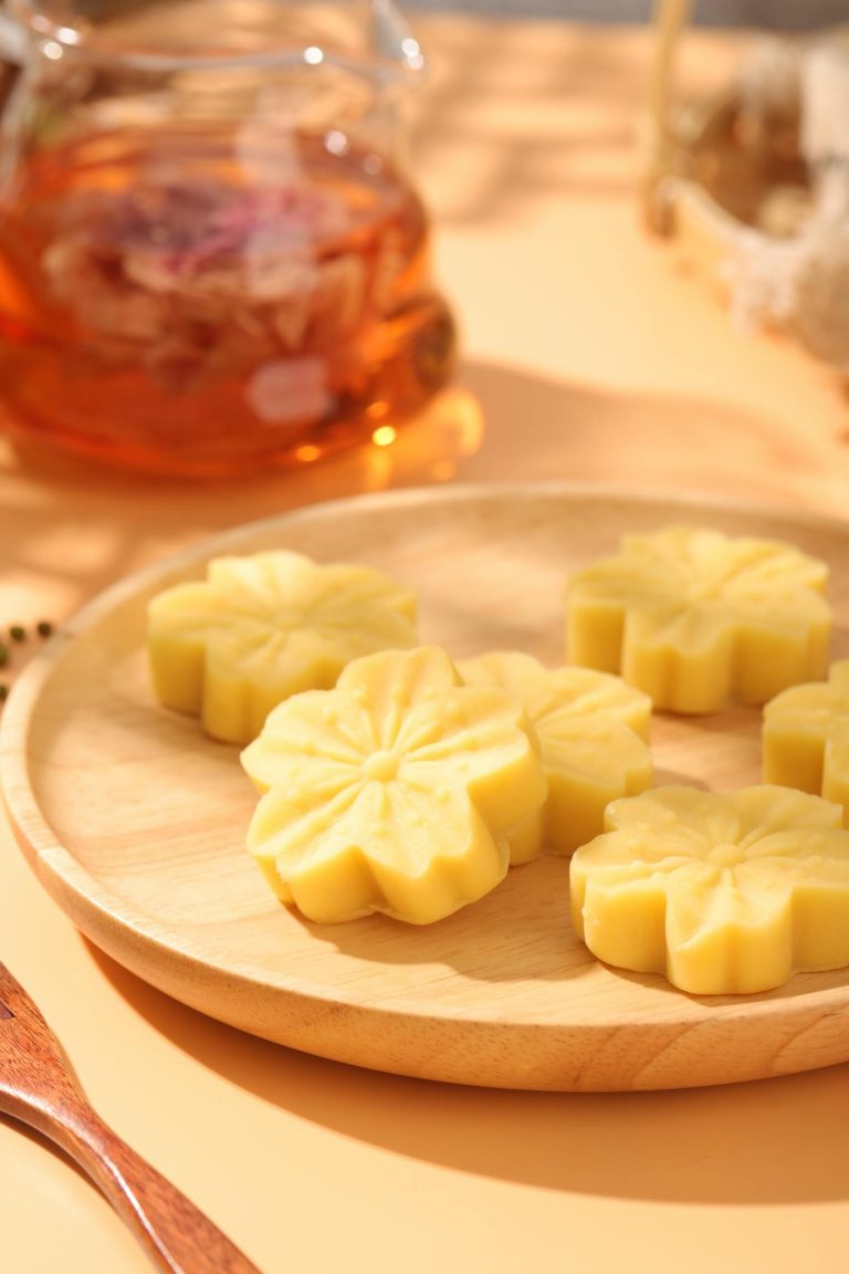 Yellow floral mooncakes on a wooden plate with tea in the background.